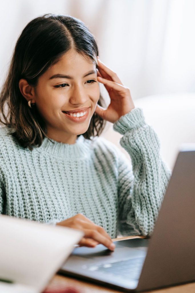 Closeup of smiling young hispanic woman looking at laptop and wearing a pastel green sweater