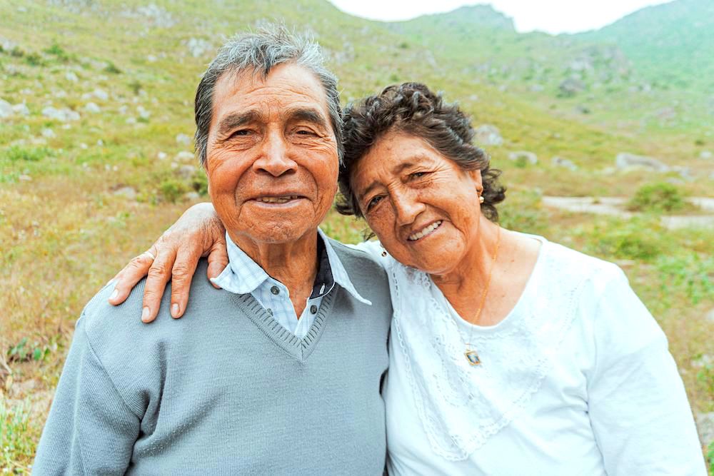 Closeup of old hispanic couple looking at camera and smiling in front of a hill.