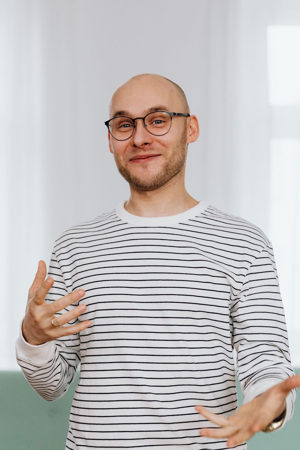 Young bald man with striped shirt and glasses smiling at camera