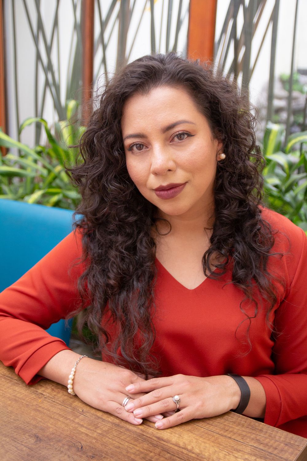 Closeup of hispanic professional woman in her 30s, long curly hair, red blouse, looking into camera.