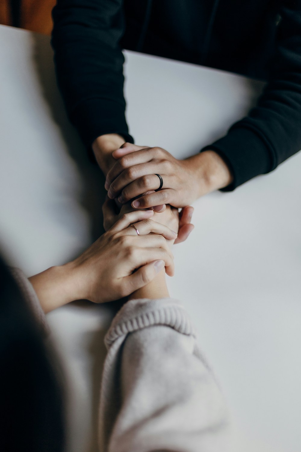 2 people clasping hands across the table in support of each other, closeup on the hands