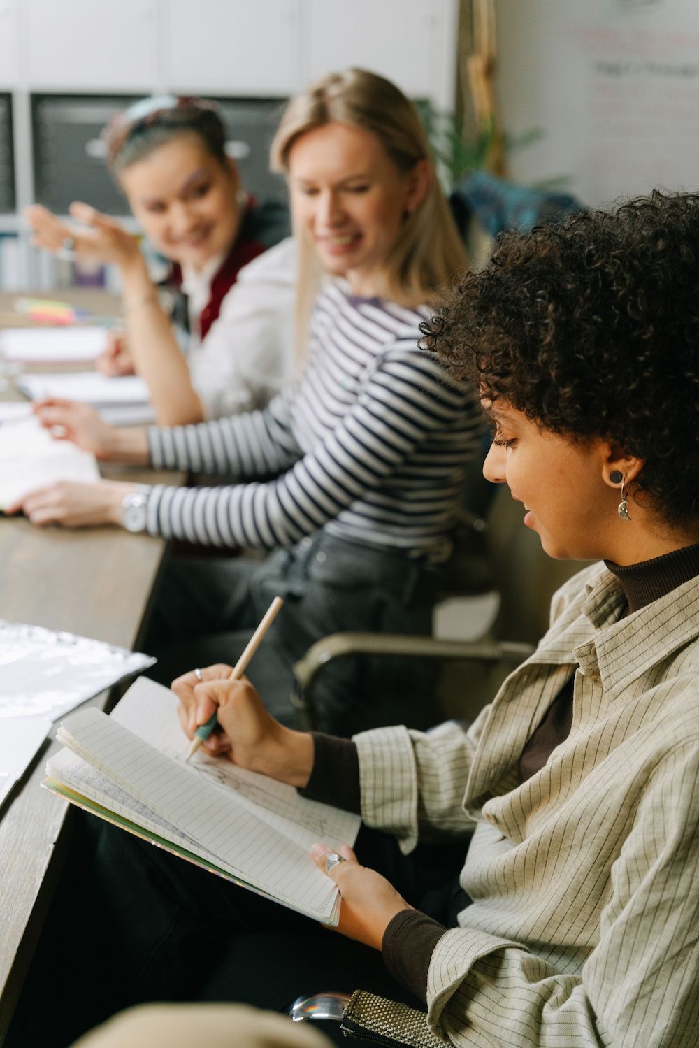 Side view of 3 female adult students writing and talking