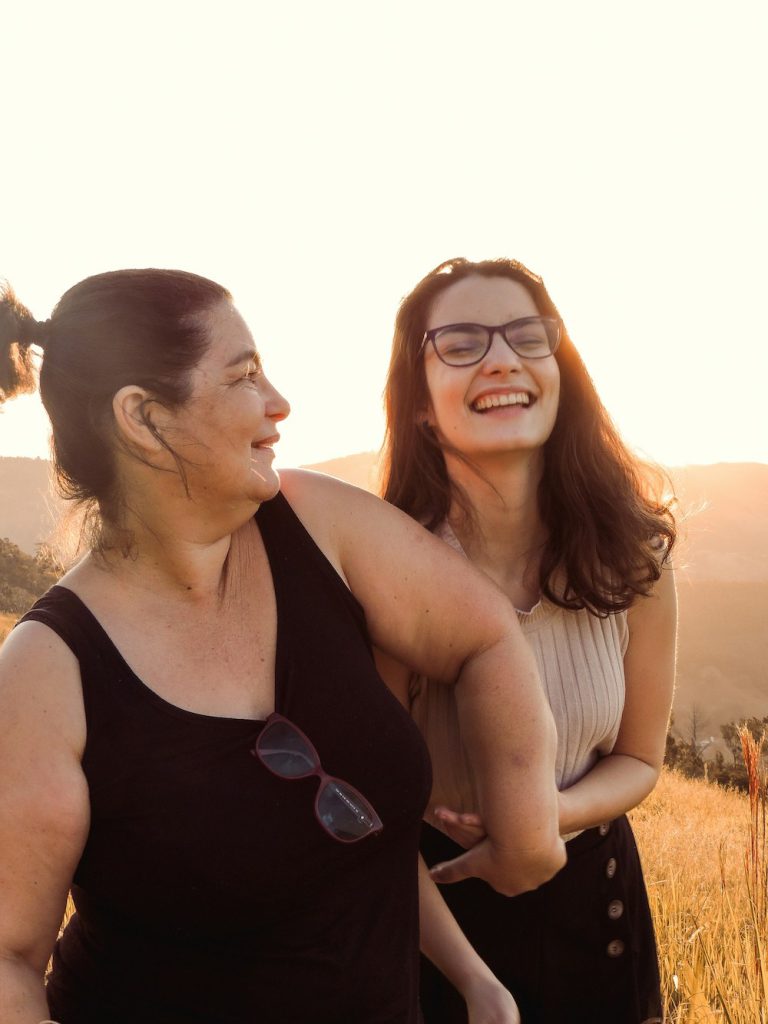 Mother and daughter walk around in a prairie at sunset laughting