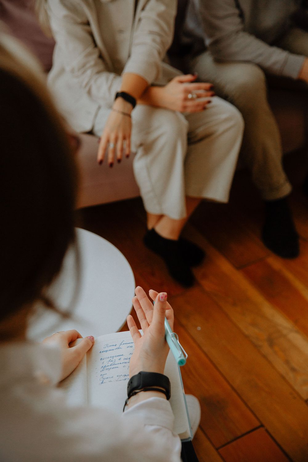 Top view of a counseling session, focus is over-the-shoulder view therapist's notebook, clients farther back and out of focus