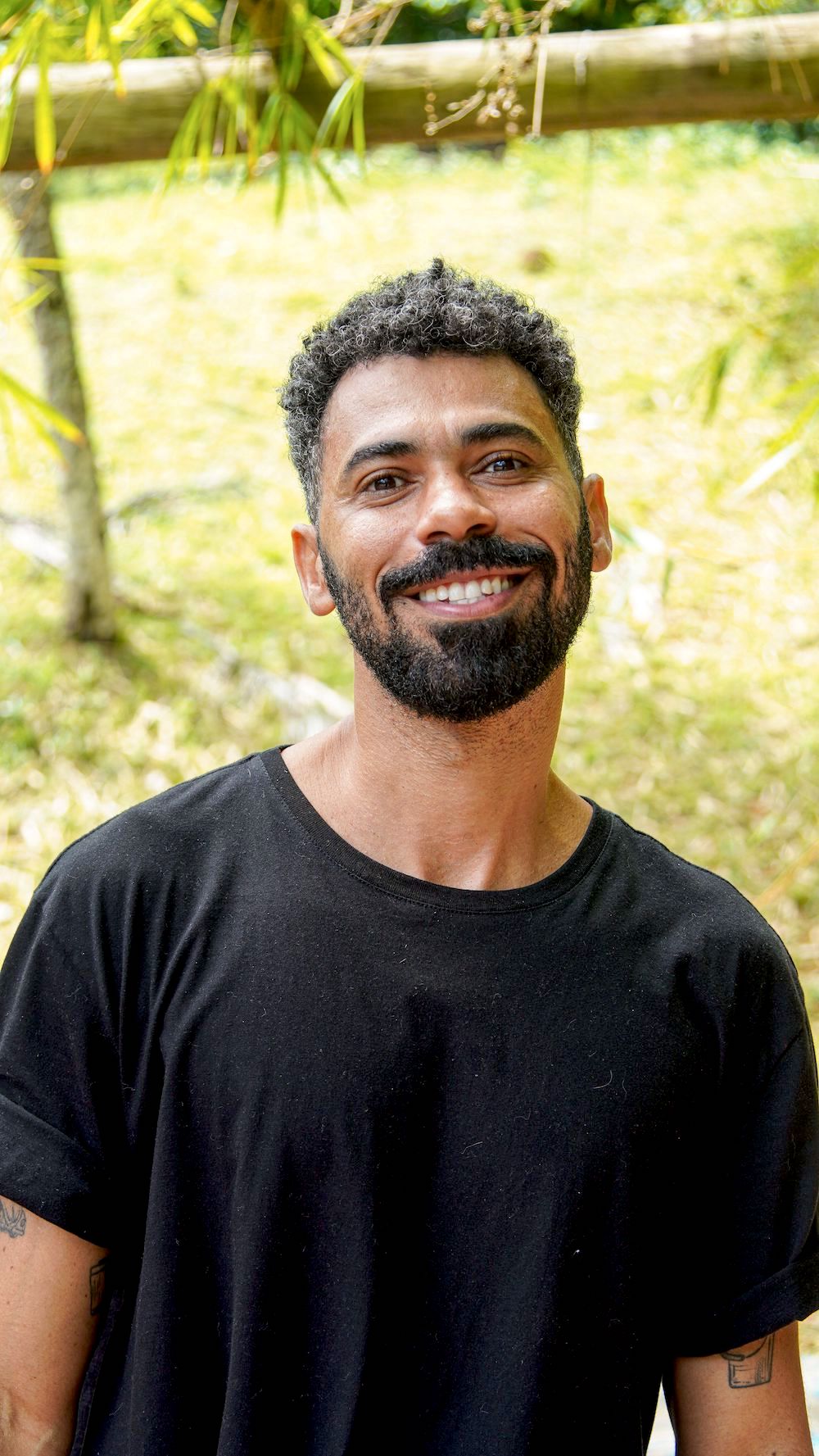 Closeup of middle-aged Brazilian man with a beard and curly hair looking at the camera, standing in a garden